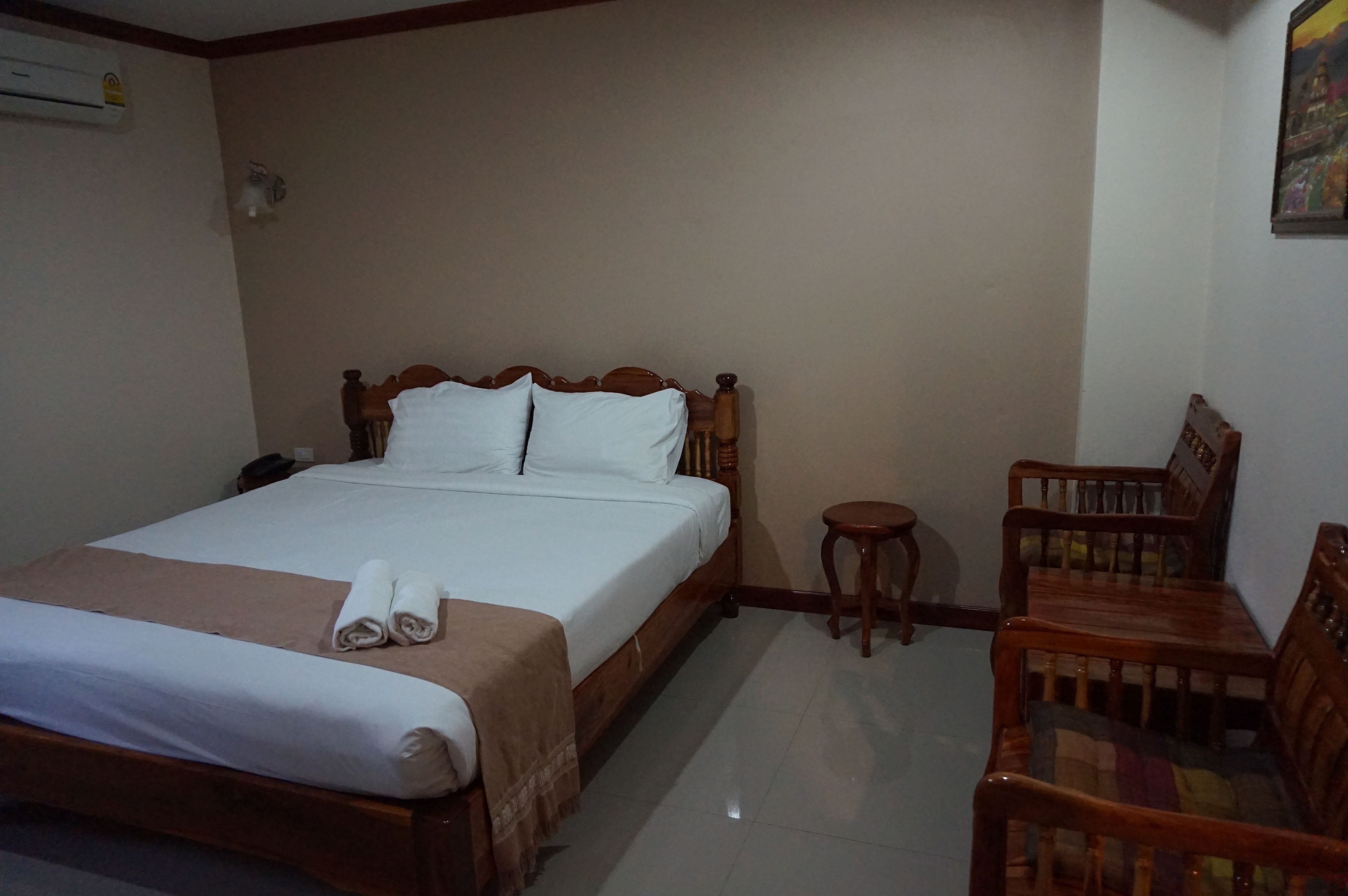Una habitación de hotel con una cama de madera, una pequeña mesa redonda y dos sillas de madera.