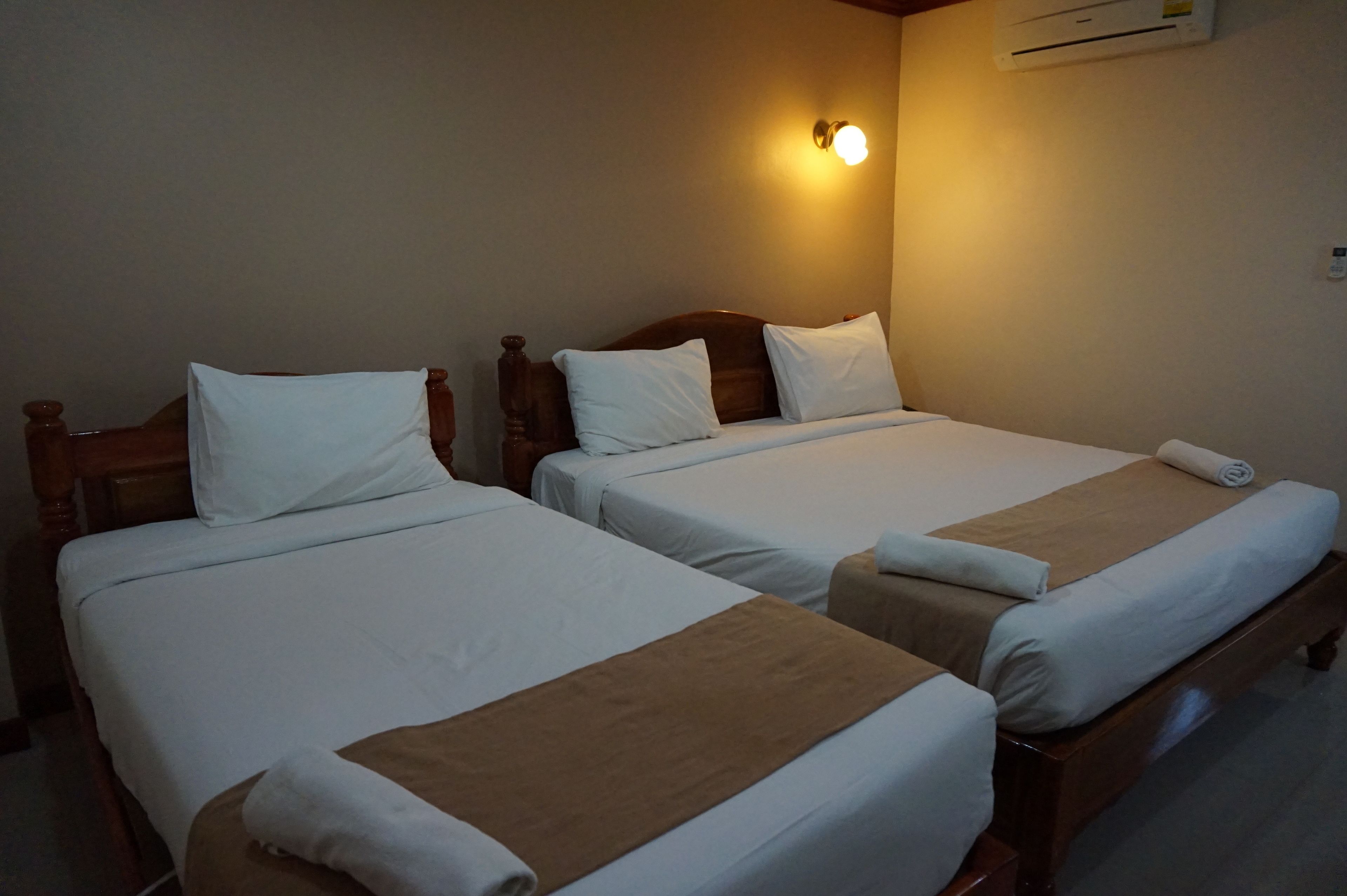 Dos camas individuales con cabeceros de madera, ropa de cama blanca y mantas marrones.