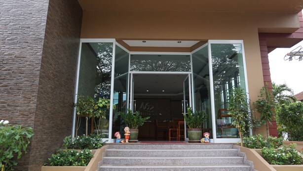 A hotel entrance with a modern design, featuring a glass facade, a set of stairs leading up to the entrance, and potted plants on either side. - NP Residence (Nakhon Phanom)