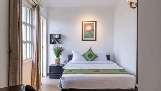 Une chambre à coucher bien rangée, avec un lit, une table de chevet et une lampe fixée au mur.
