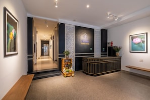 A reception area with a reception desk, a bench, a decorative plant, and framed artwork on the walls. - Purple Hue Charming Riverside Hotel (Hue)