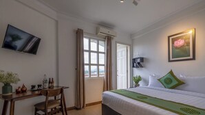 Une chambre d’hôtel comprenant un lit, un bureau, une chaise, une télévision, une fenêtre avec des rideaux et un tableau encadré au mur.