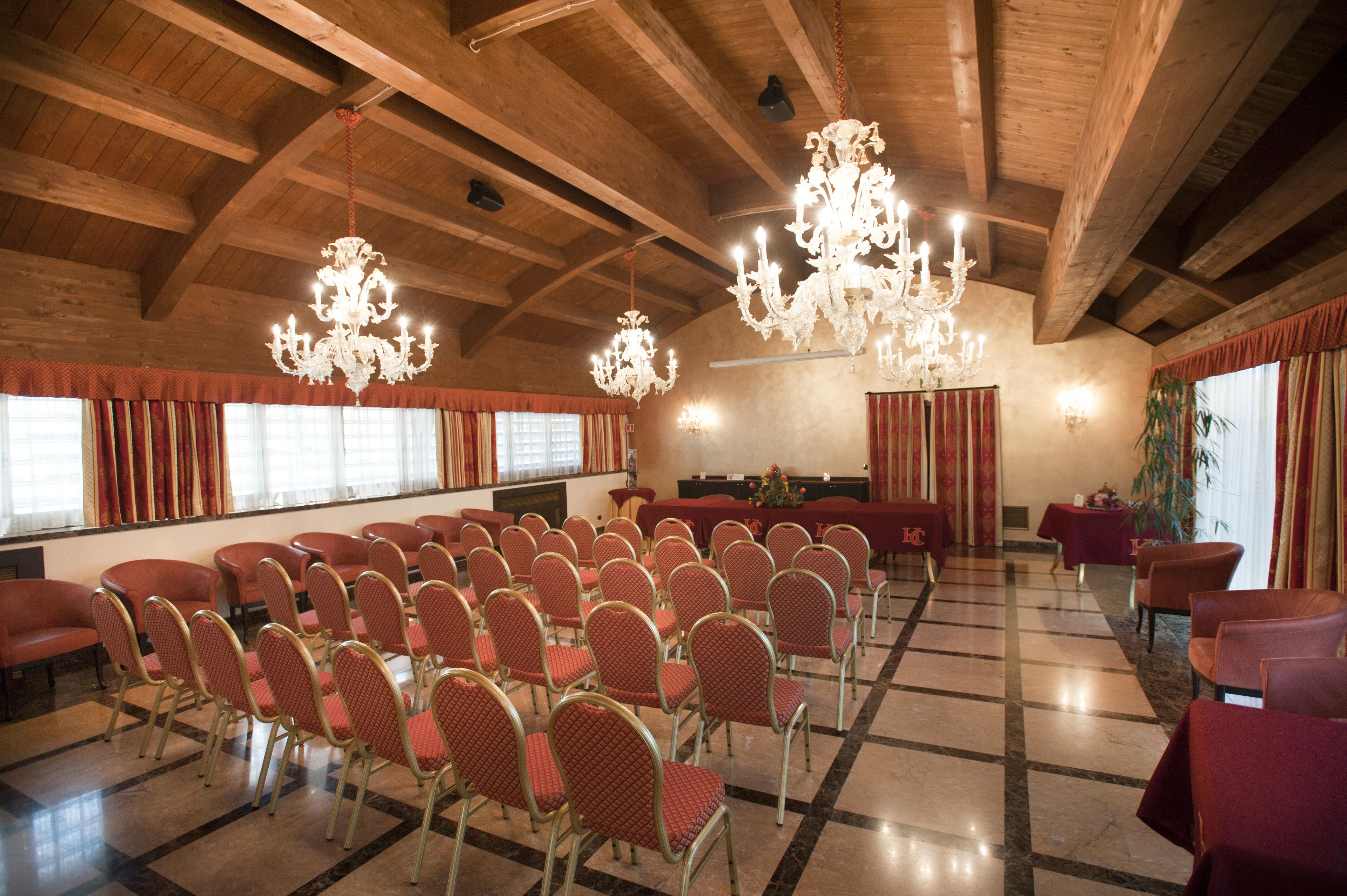 A conference room with rows of red chairs, a stage with a piano, and chandeliers.