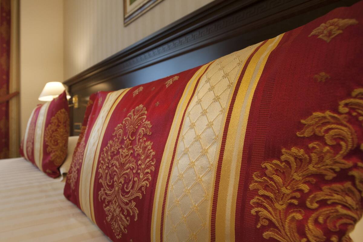 Habitación de hotel con una cama grande, cabecera con estampado rojo y dorado, y ventana con cortinas.