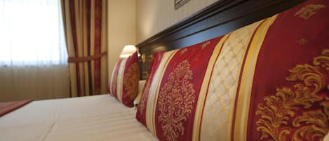 A hotel room with a large bed, red and gold patterned headboard, and a window with curtains.