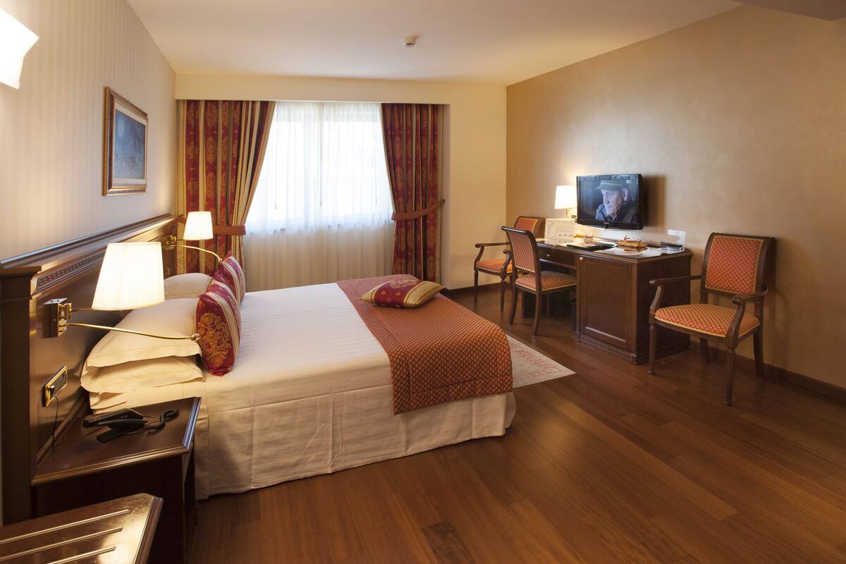 Una habitación de hotel con cama, escritorio, televisor y sillas.