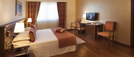 A hotel room with a bed, desk, TV, and chairs.
