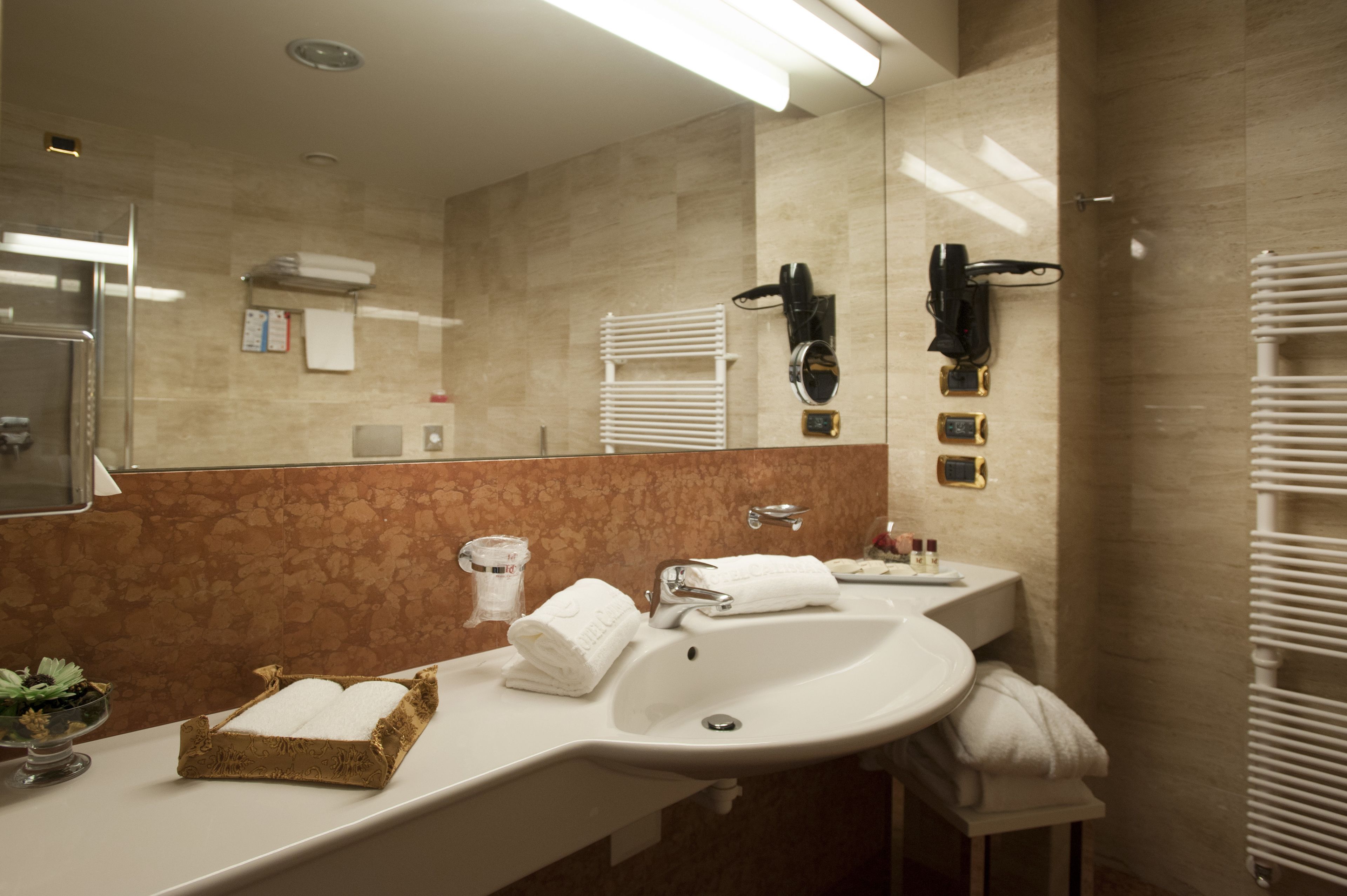 A modern bathroom with a large mirror, two sinks, a towel rack, and a heated towel rail.