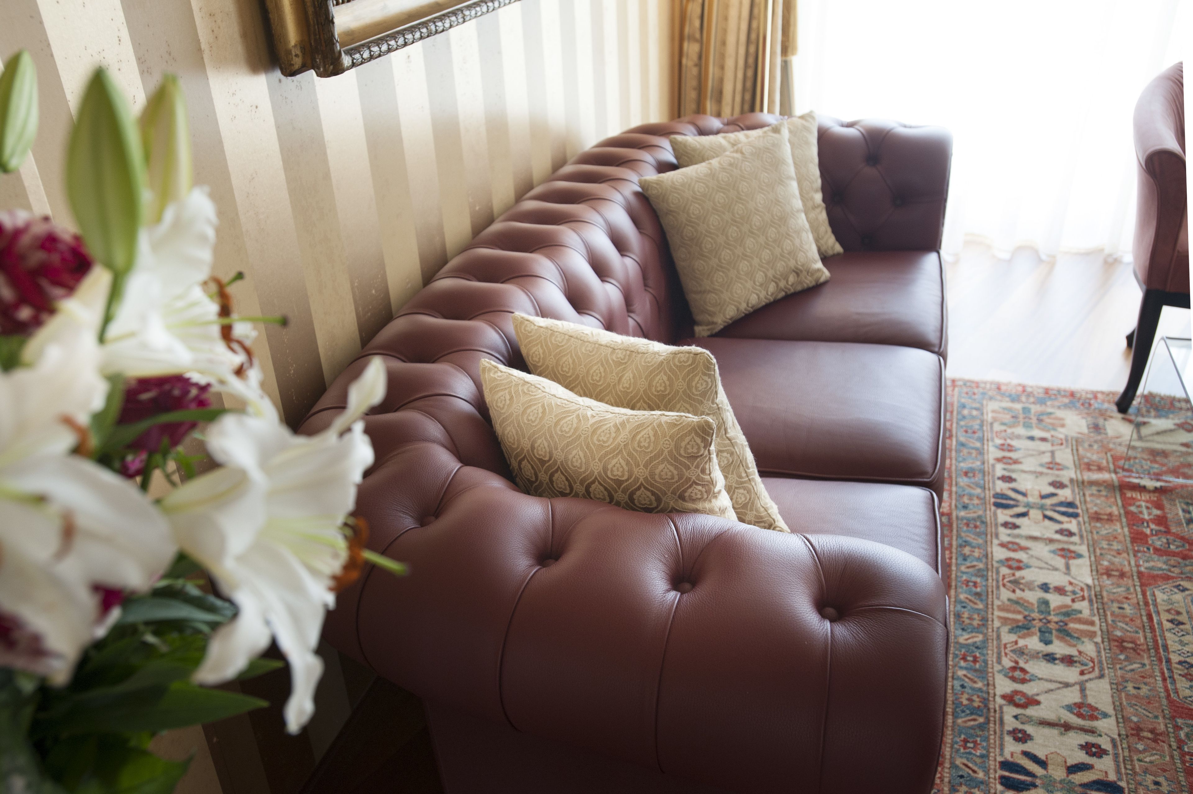 A brown leather sofa with patterned cushions, a striped wall, and a floral arrangement.