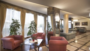 A spacious lobby with a marble floor, red sofas, a coffee table, and large windows with curtains. - Hotel Calissano (Alba)