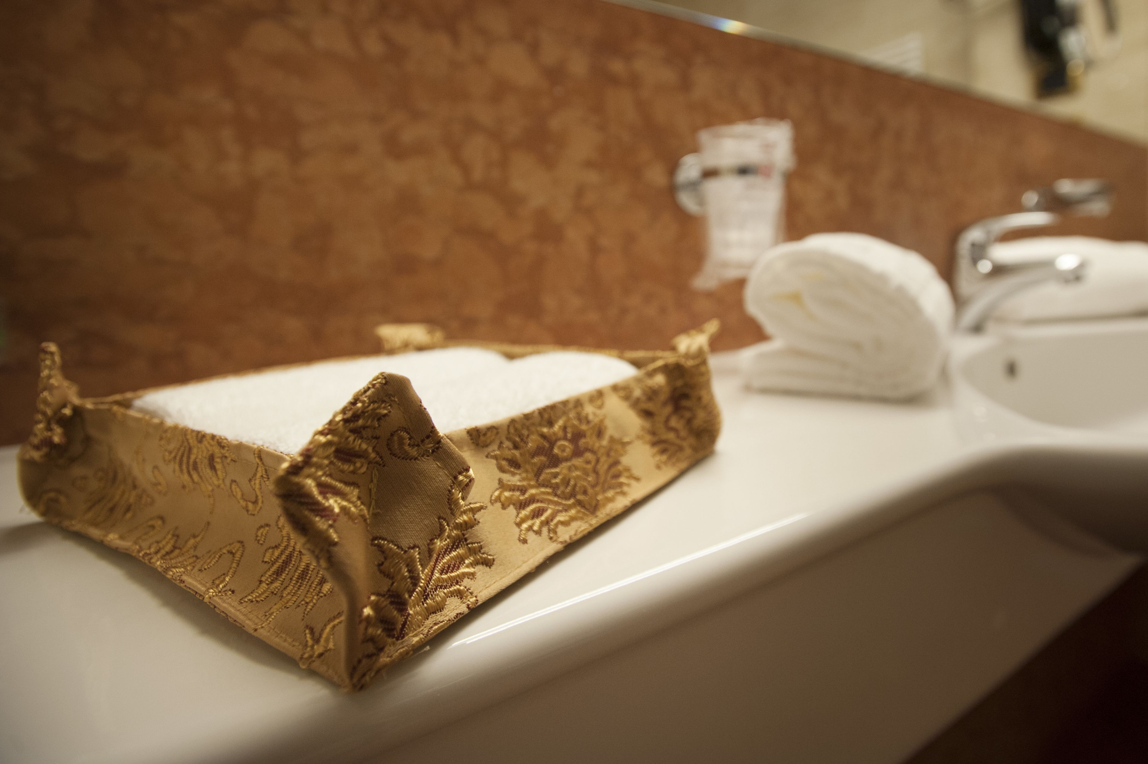 Un baño con un sujetarropas dorado decorativo, un lavamanos blanco y una toalla doblada sobre el mostrador.