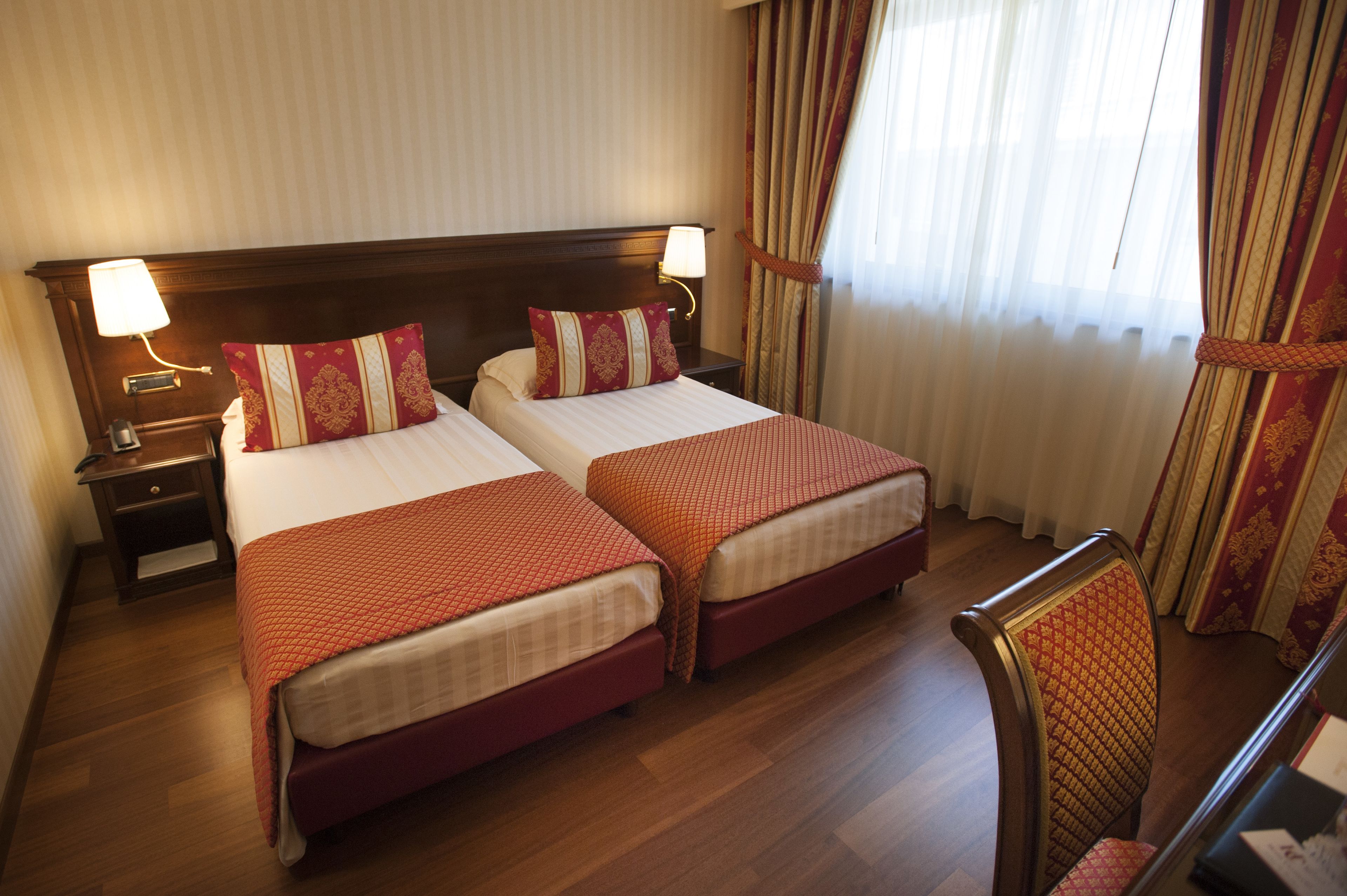 Habitación de hotel con dos camas, cabeceros de madera y una mesita de noche con lámpara.