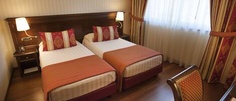 Habitación de hotel con dos camas, cabeceros de madera y una mesita de noche con lámpara.