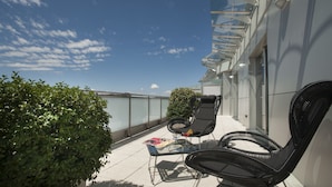 A rooftop terrace with two black wicker chairs, a glass table, and a small potted plant. - Hotel Calissano (Alba)