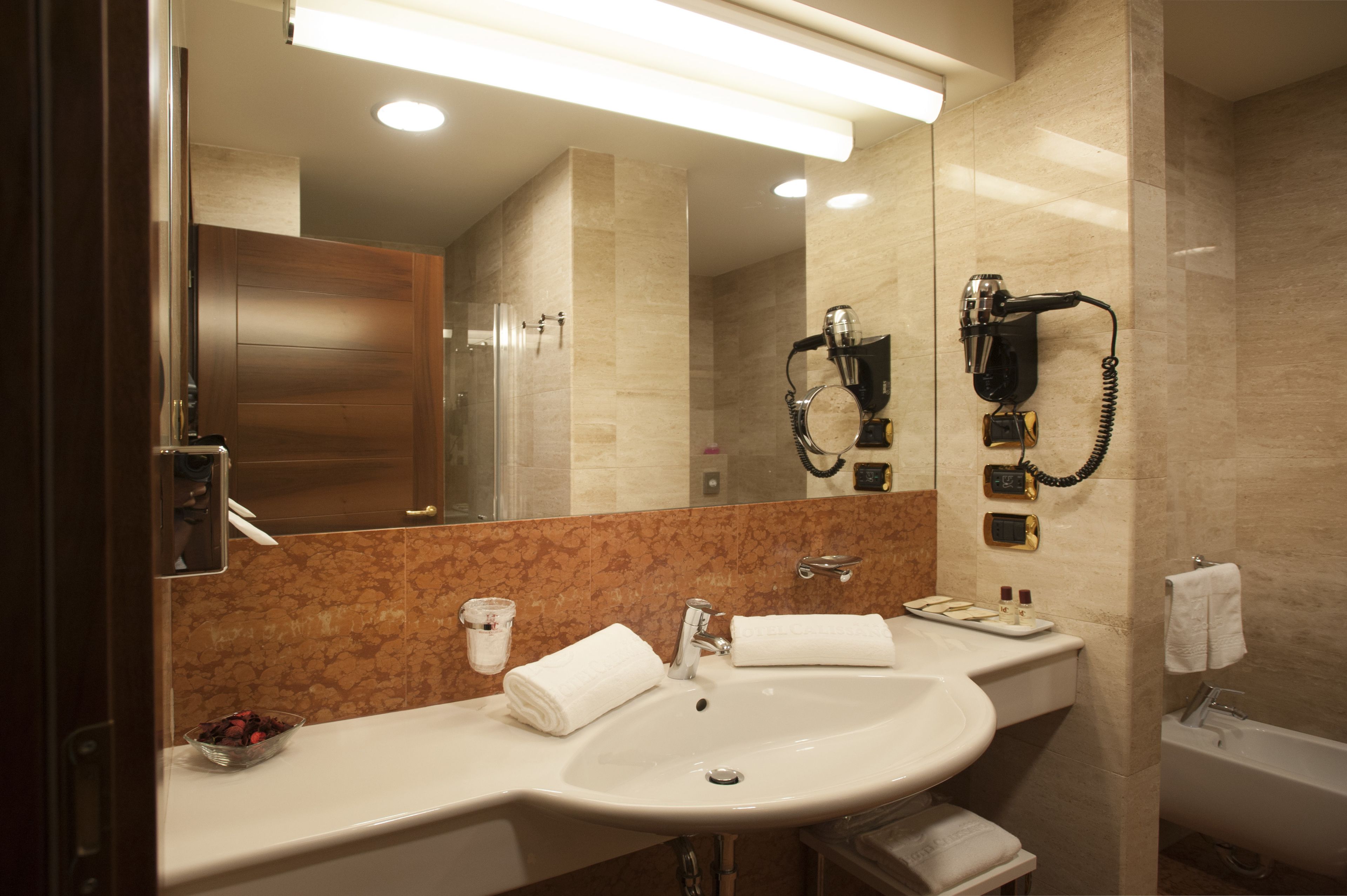 Ein modernes Badezimmer mit großem Spiegel, Waschbecken, Fön und Badewanne.