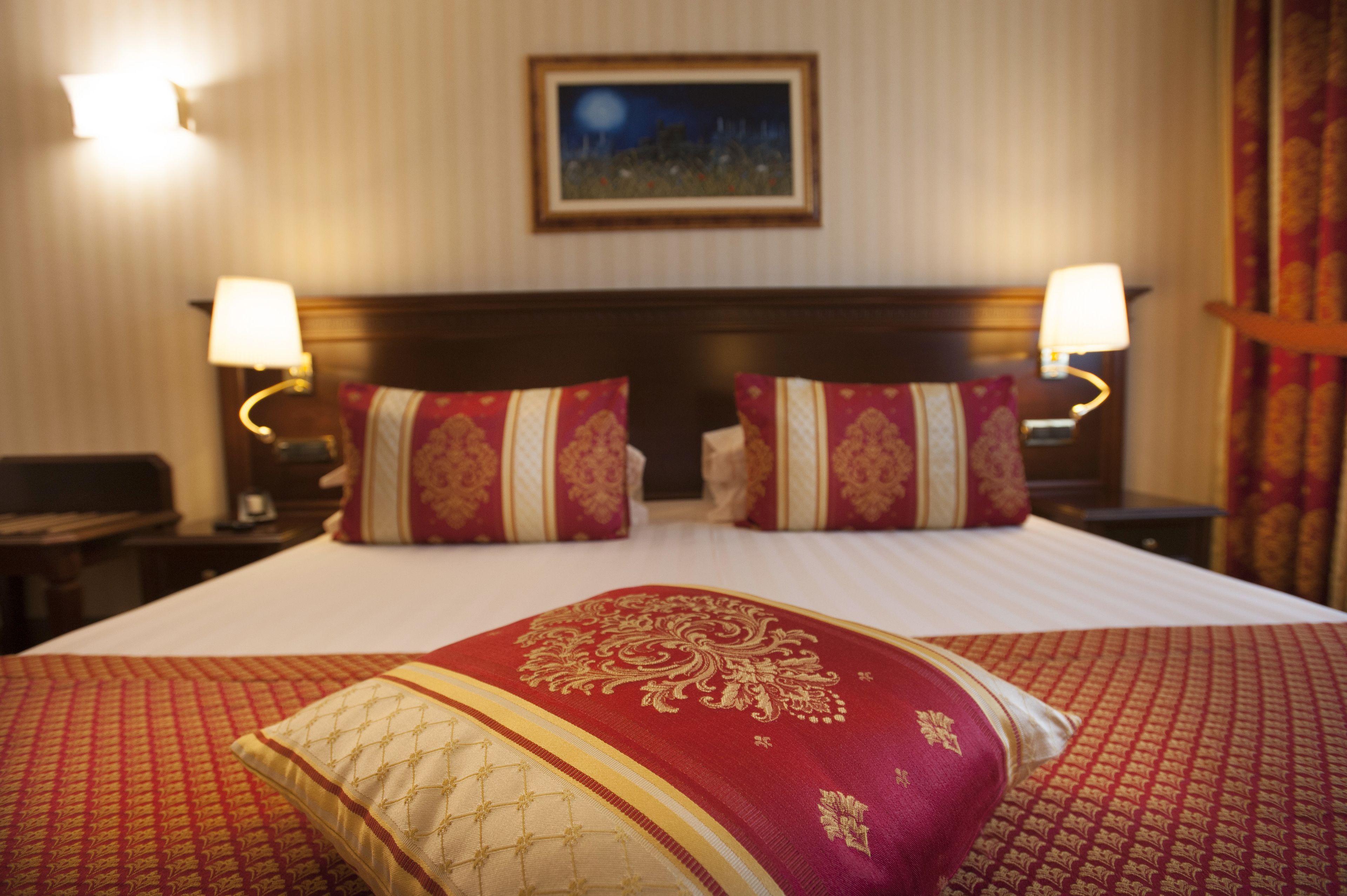 A hotel room with a large bed, two bedside lamps, and a framed picture on the wall.