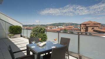 A balcony with a table set for dining, overlooking a cityscape with buildings and a mountain in the distance.