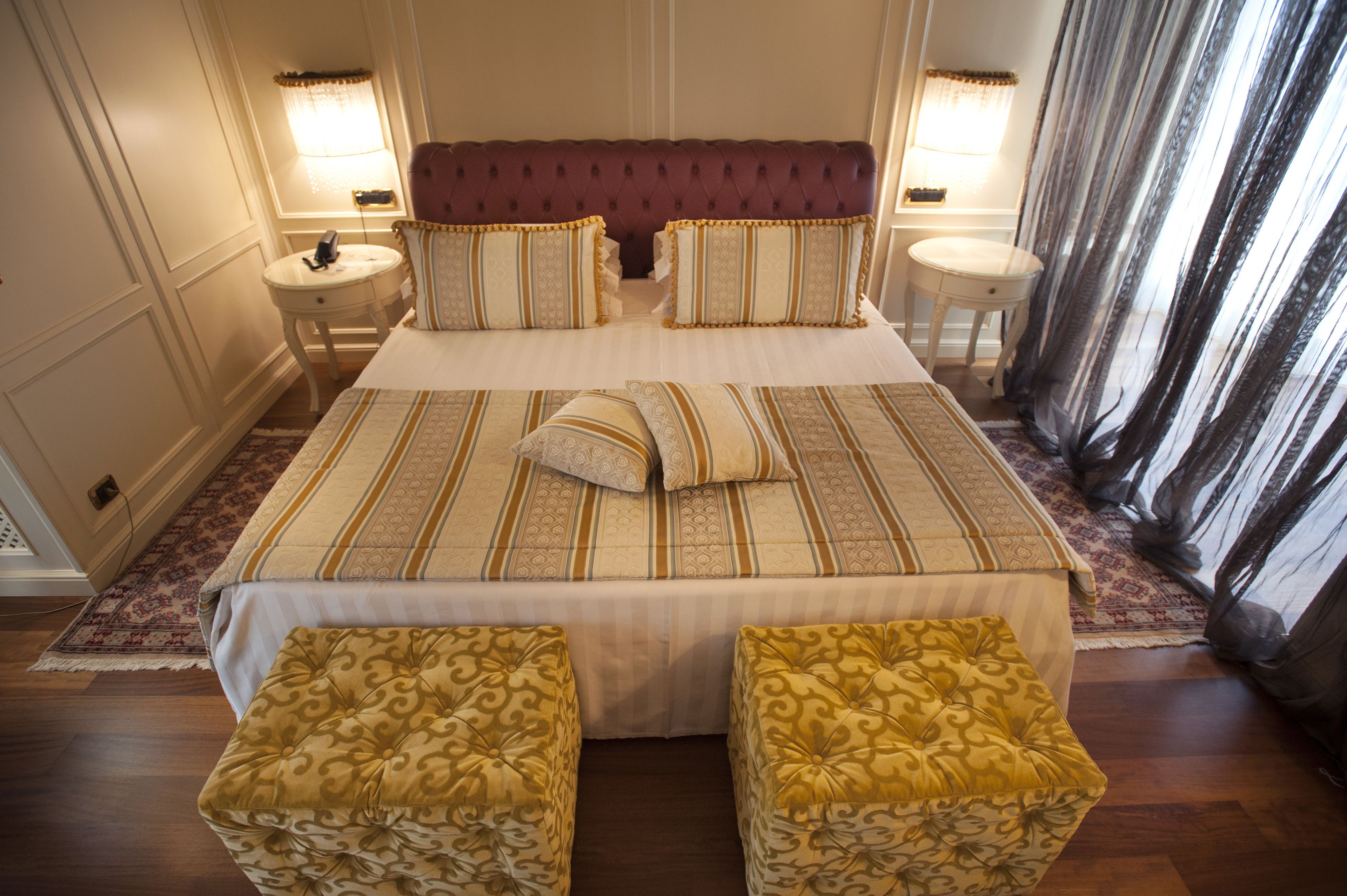 A hotel room with a large bed, two bedside tables, a red upholstered headboard, and a patterned bedspread.
