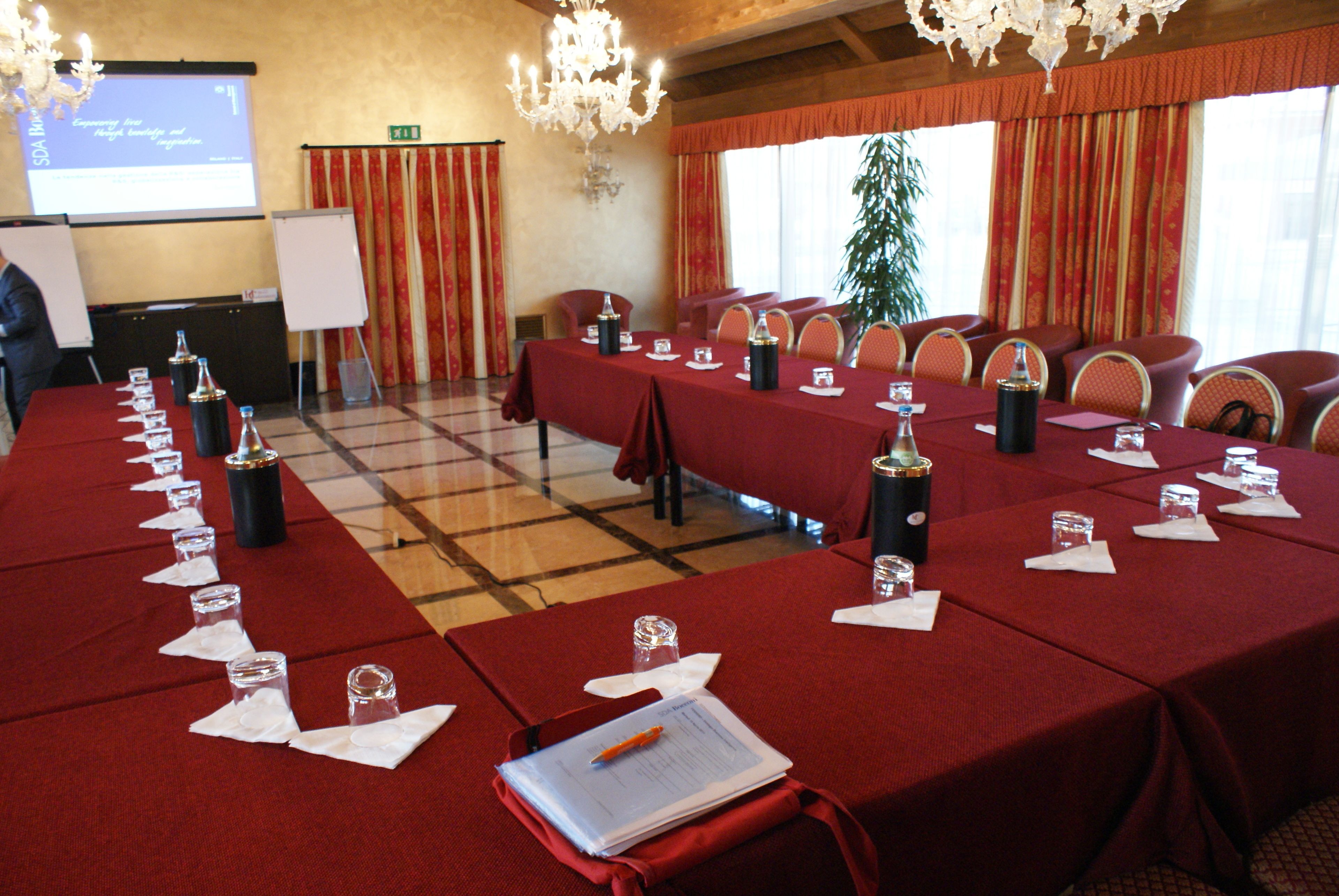 Een vergaderruimte met een lange tafel, klaar voor een vergadering, voorzien van naambordjes, waterglazen en een projectorscherm waarop een presentatie wordt getoond.