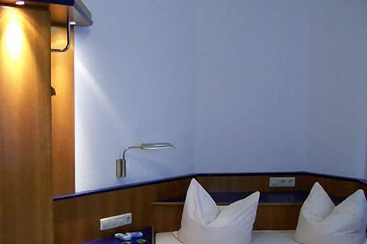 A hotel room with two beds, a bedside table, a lamp, and a wooden headboard.