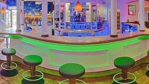 A bar area with a curved counter, green bar stools, and a ceiling with wooden beams. - Shape Sport Hotel (Winsen (Luhe))