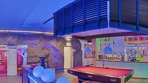 A pool table with a neon-lit edge, a wooden bench, and a bar area with a counter and stools. - Shape Sport Hotel (Winsen (Luhe))