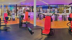 A modern gym with various exercise machines, including treadmills and weight stations, arranged in a spacious layout with large windows. - Shape Sport Hotel (Winsen (Luhe))