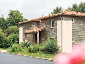 A two-story wooden house with a tiled roof, surrounded by greenery and a paved road. - Le Saint Pierre (Moncoutant-sur-Sèvre)