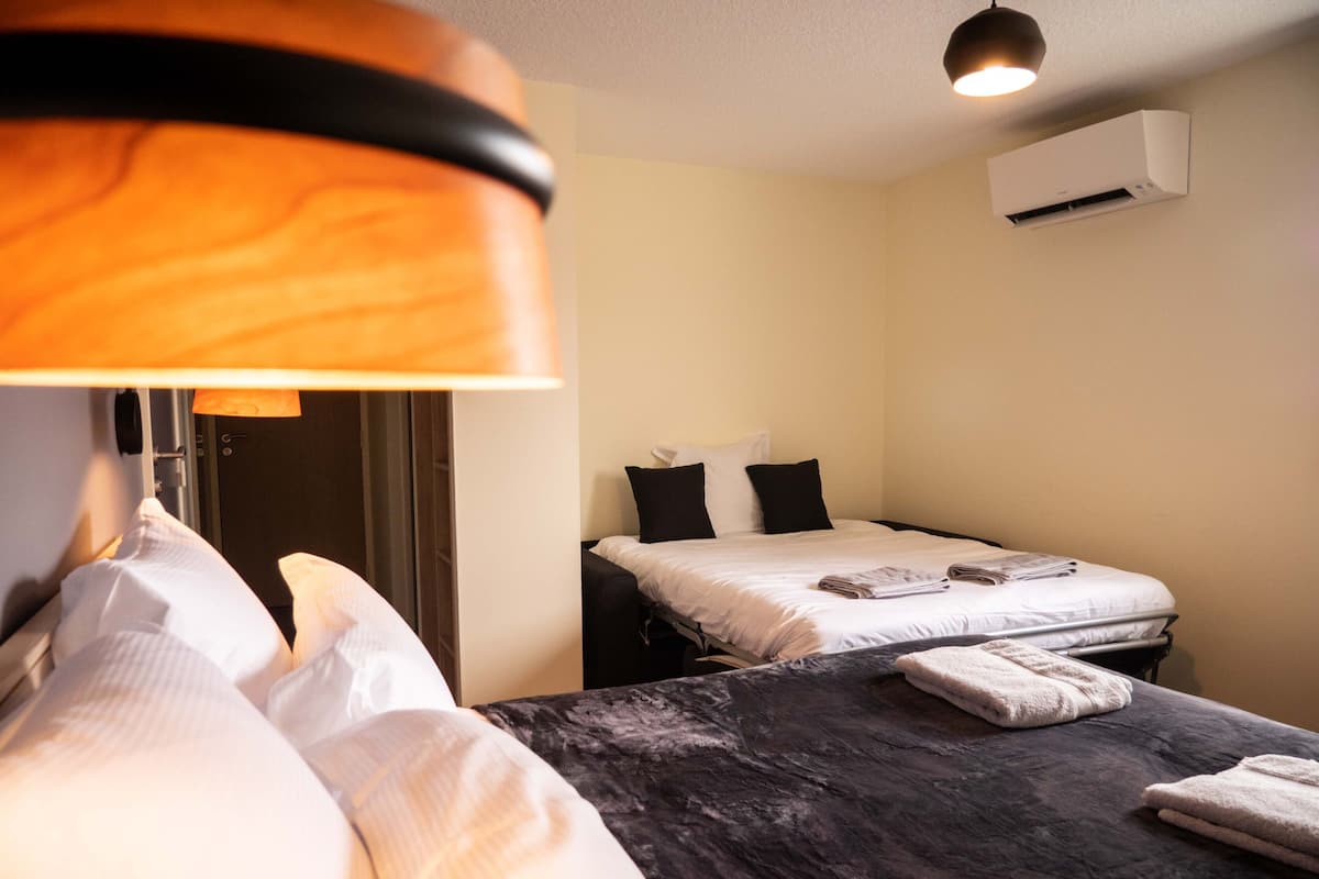 A hotel room with a bed, a desk, and a chair. There is a lamp on the desk and a window in the room.