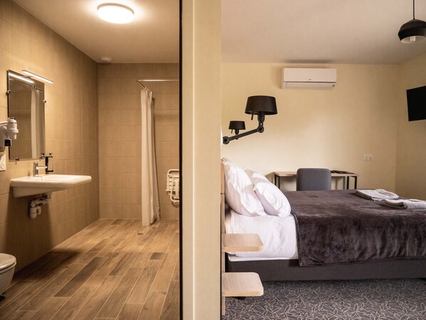 A hotel room with a shower, sink, bed, bedside table, and a TV mounted on the wall. - Le Saint Pierre (Moncoutant-sur-Sèvre)