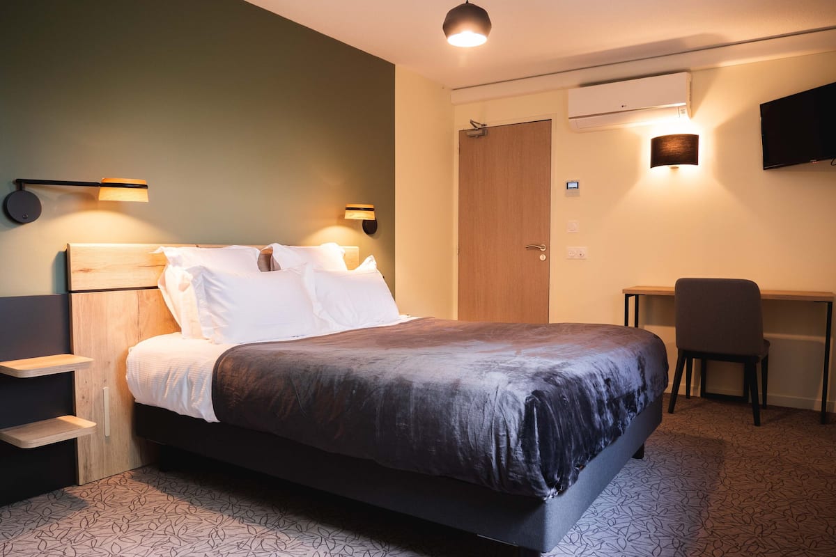 A modern hotel room with a bed, bedside tables, a desk, and a chair.