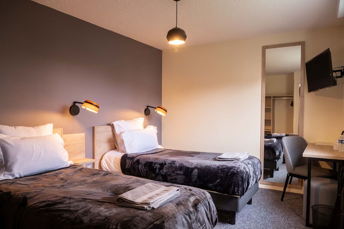 A hotel room with two beds, a desk, and a TV.
