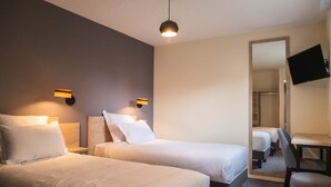 Habitación de hotel con dos camas, un escritorio, una silla, un televisor montado en la pared y un espejo.