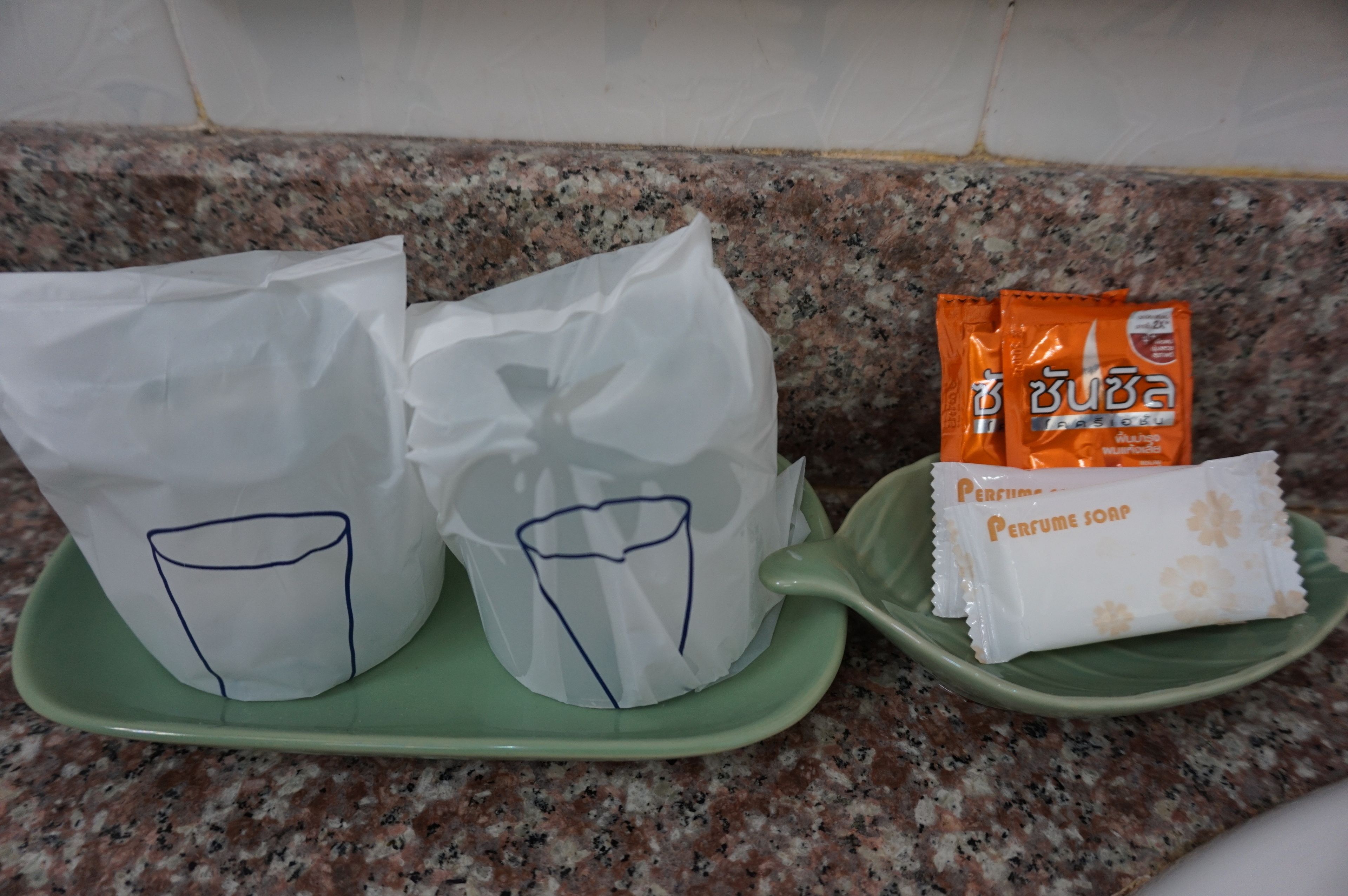 Two paper cups with blue outlines on a green tray, and two packets of soap on another green tray.