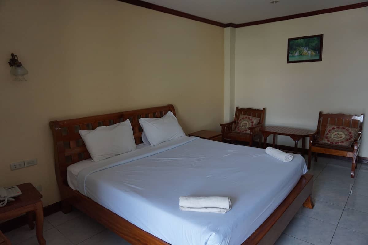 A hotel room with a large bed, two wooden chairs, a small table, and a painting on the wall.