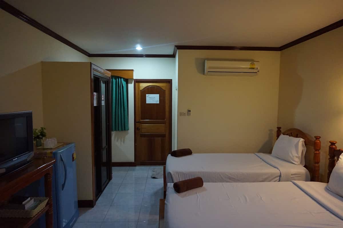 A hotel room with two beds, a television, a refrigerator, and an air conditioning unit.