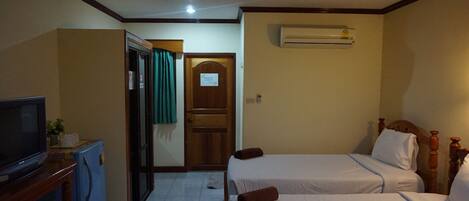 A hotel room with two beds, a television, a refrigerator, and an air conditioning unit.