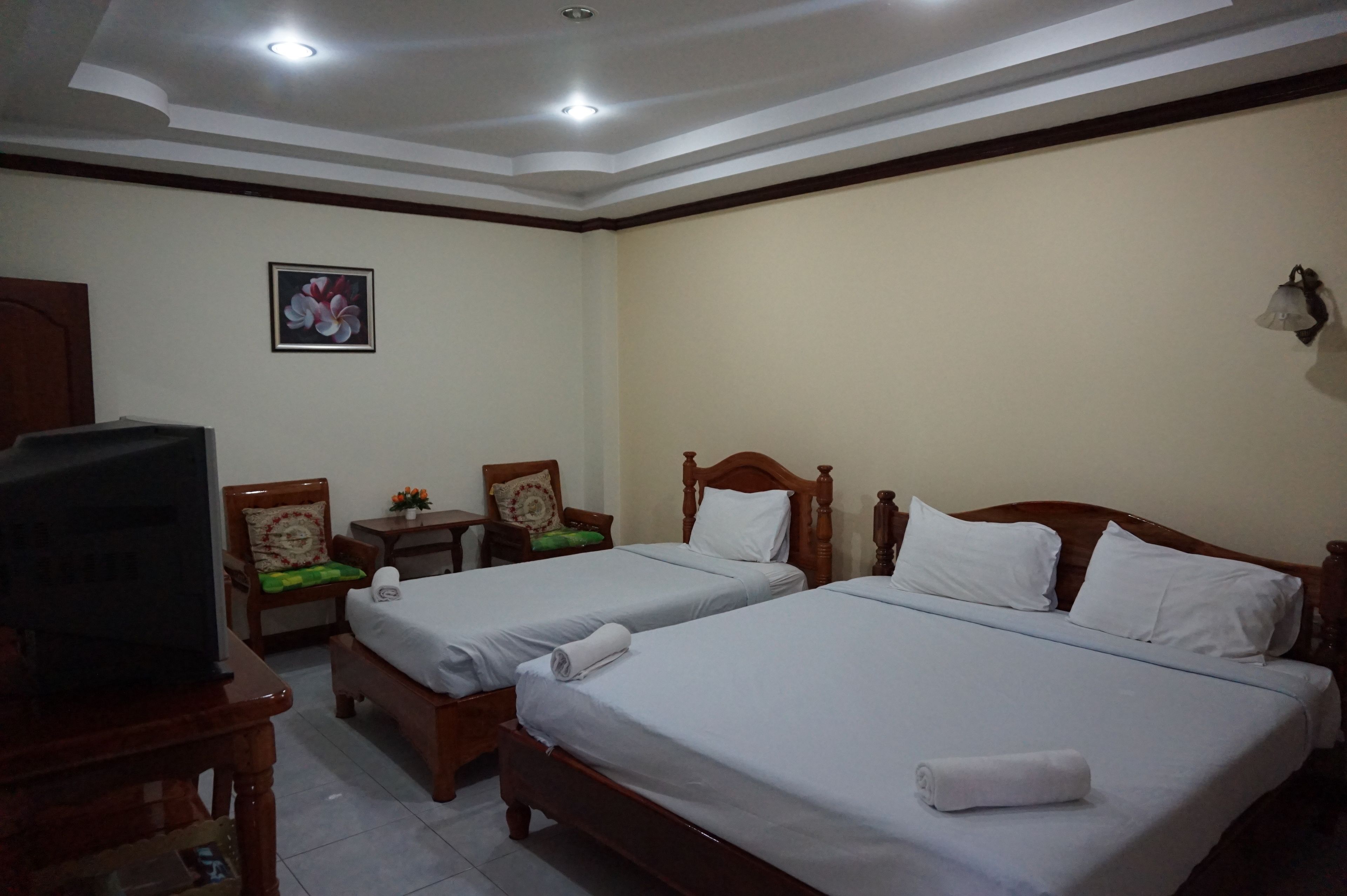 Habitación de hotel con dos camas individuales, una televisión, una mesita con una silla y una lámpara de pared.