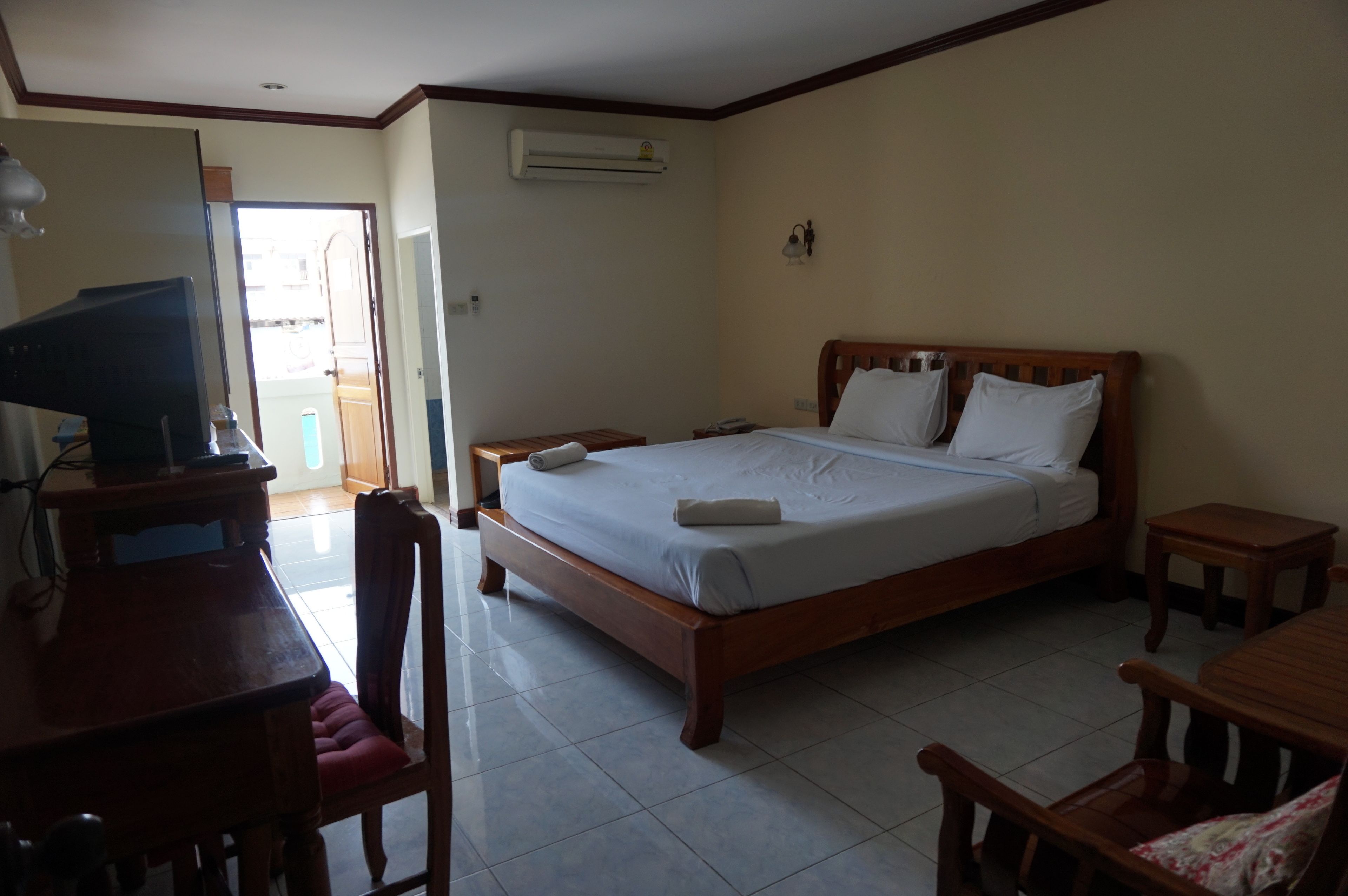 A bedroom with a bed, bedside tables, a desk with a chair, and an air conditioning unit.