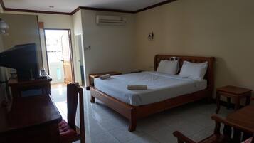 A bedroom with a bed, bedside tables, a desk with a chair, and an air conditioning unit.