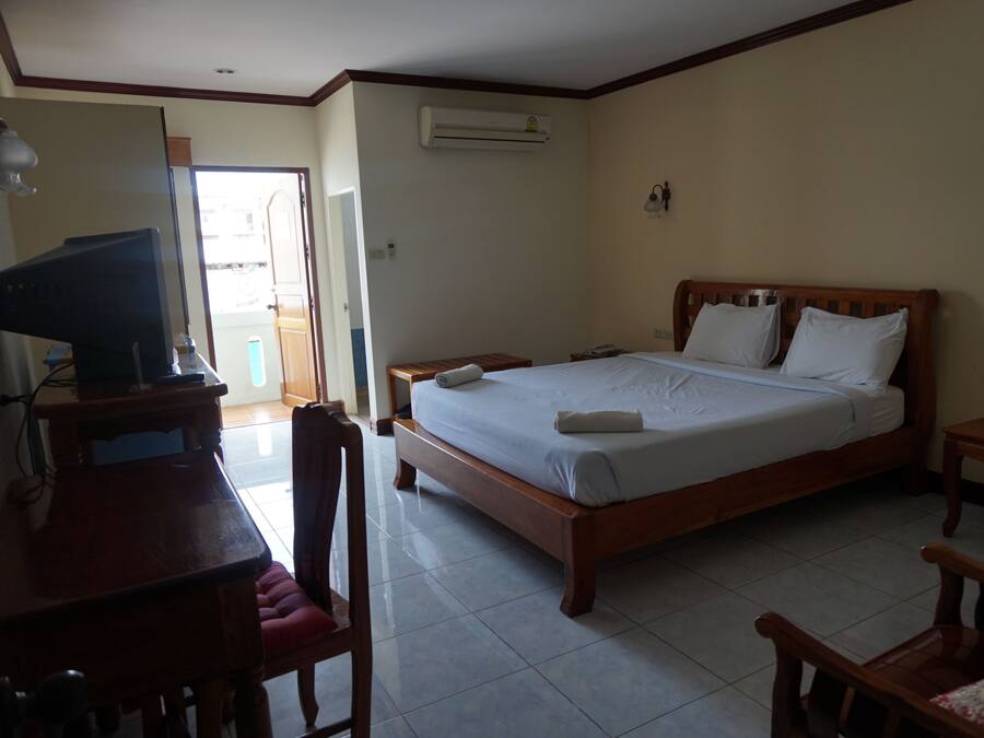 A bedroom with a bed, bedside tables, a desk with a chair, and an air conditioning unit.