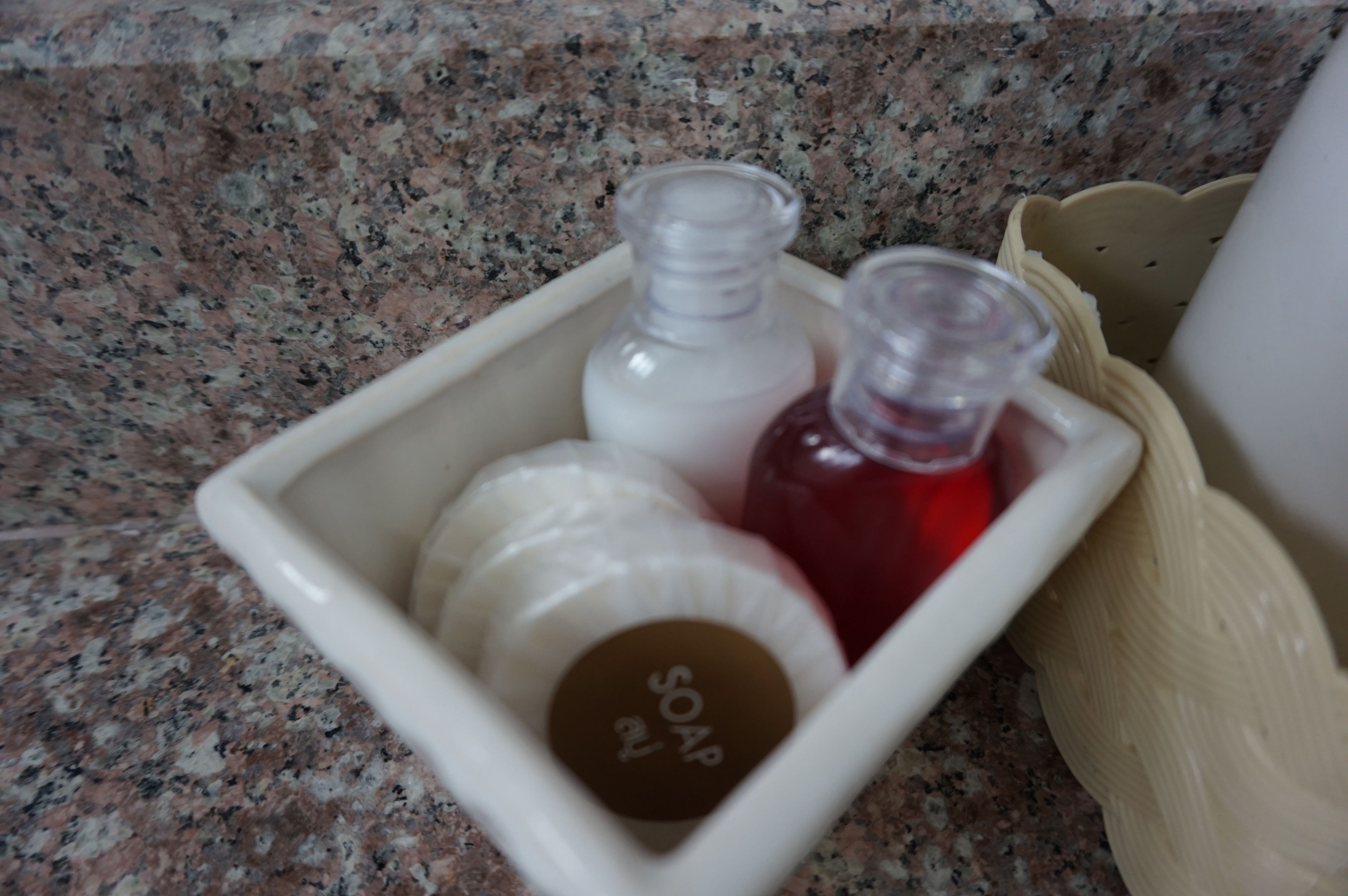 A white soap dish with three bottles of soap on a granite countertop.