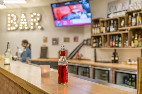 A bar with a counter, a TV screen, and shelves of bottles. - Hostel Art & Style (Singen)