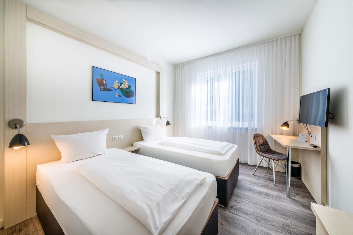 Habitación de hotel con dos camas, un escritorio, una silla, un televisor y un cuadro en la pared.
