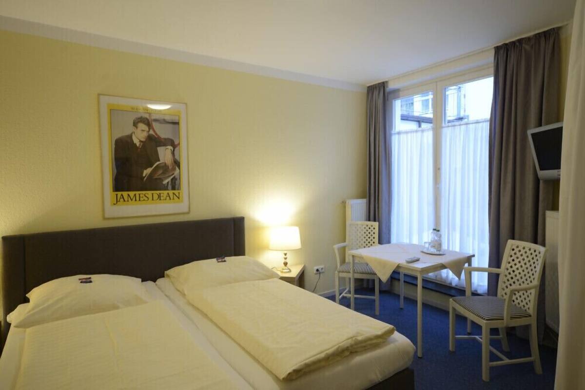 A hotel room with two beds, a table with chairs, a TV, and a poster on the wall.