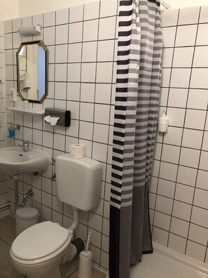 A bathroom with a toilet, sink, mirror, and striped shower curtain. - Alpha Hotel-Pension (Hamburg)