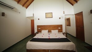 Habitación de hotel con techo de madera, cama con ropa blanca, mesita de noche pequeña y velador.