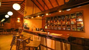 Zona de bar con taburetes de madera, una barra y una pared llena de botellas de licores.