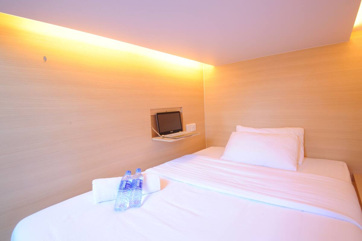 A hotel room with a bed, pillows, a flat-screen TV mounted on the wall, and two bottles of water on the bed.