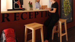 A reception area with a desk, two stools, a red wall, a map of Sri Lanka, and a red backpack on the floor. - Star Anise Boutique Capsule (Colombo)